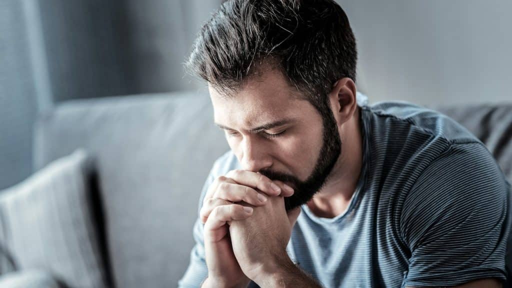 A sad man sitting on a couch with his eyes closed. 