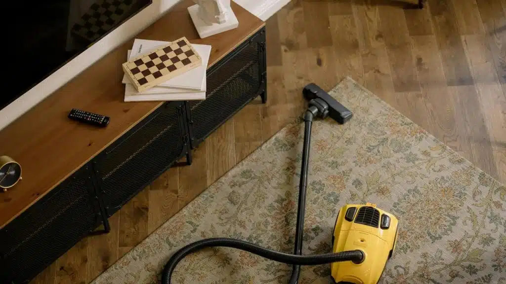 A yellow vacuum cleaner on a patterned rug near a wooden TV stand.