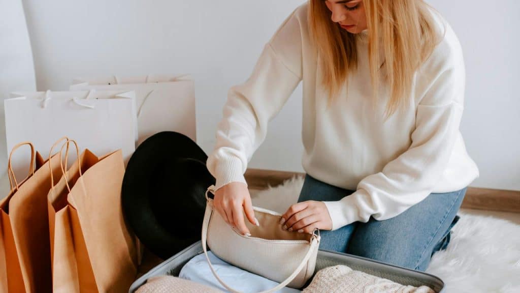 A woman kneeling and packing clothes into a suitcase.