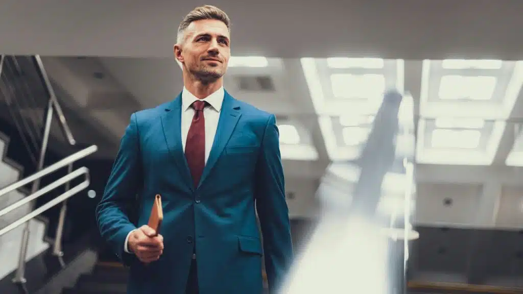 A man in a blue suit walking down a flight of stairs with a wallet in his hand.