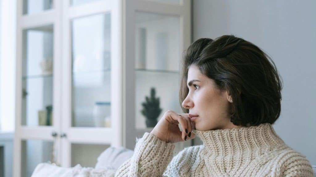 A person in a chunky sweater sitting and looking thoughtfully to the side.