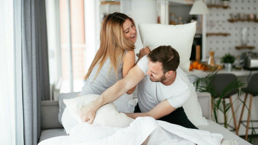A man and a woman are having a playful pillow fight on a bed or couch.