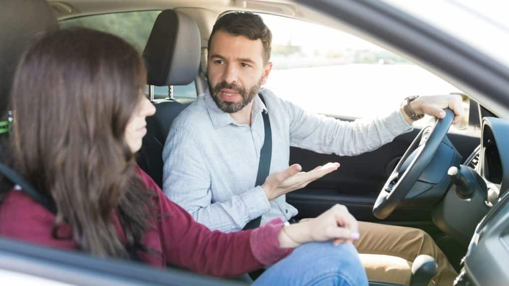 A man driving a car is turned to the passenger, gesturing and speaking in an animated discussion.