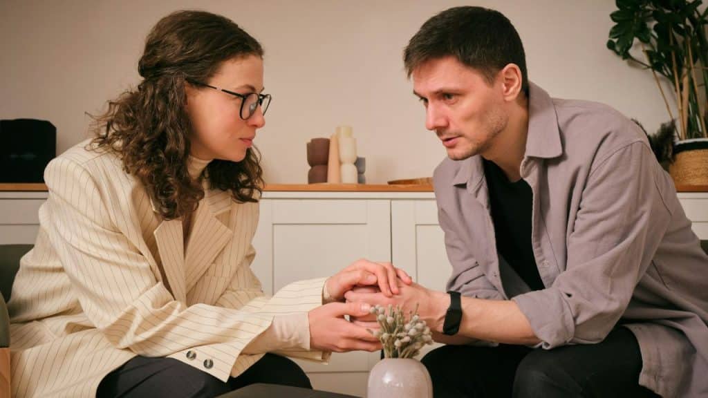 Woman holding a man's hands while they look at each other seriously indoors.