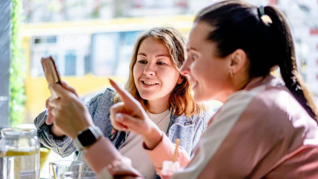 A pair of women smiling and looking at a phone together.