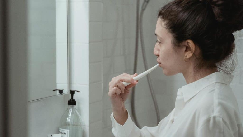 A woman brushing her teeth in front of a bathroom mirror.