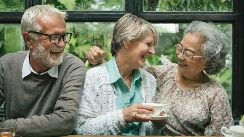 Three seniors sit together laughing, with one holding a teacup and saucer.