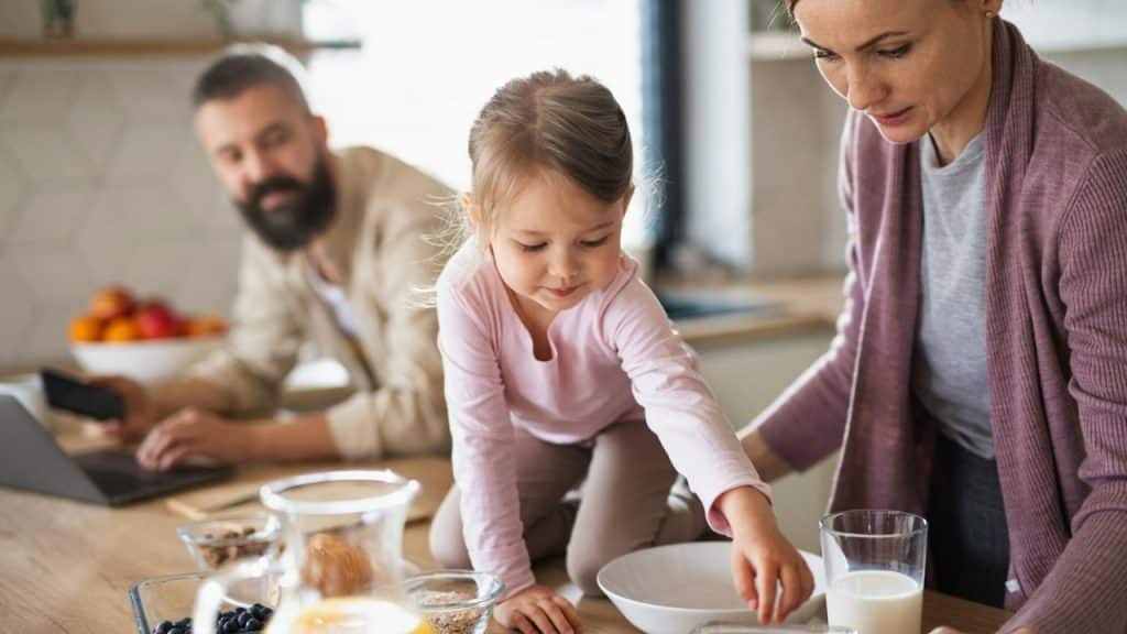 A woman and a small girl are on a kitchen counter preparing food; a man is in the background.
