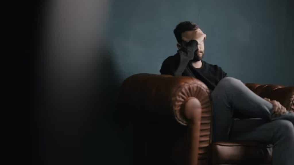 A man sitting on a couch in deep thought, soft natural lighting, realistic editorial photo.