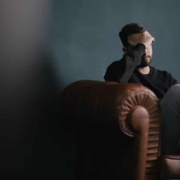 A man sitting on a couch in deep thought, soft natural lighting, realistic editorial photo.