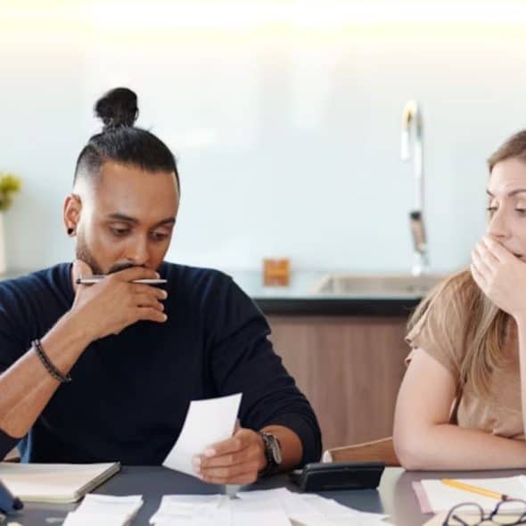 A couple sitting at a kitchen table with bills spread out, looking concerned