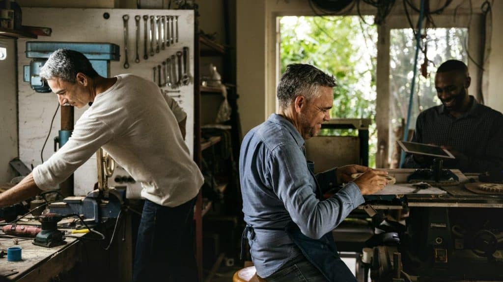 Three diverse men are working on projects in a well-lit workshop or makerspace.
