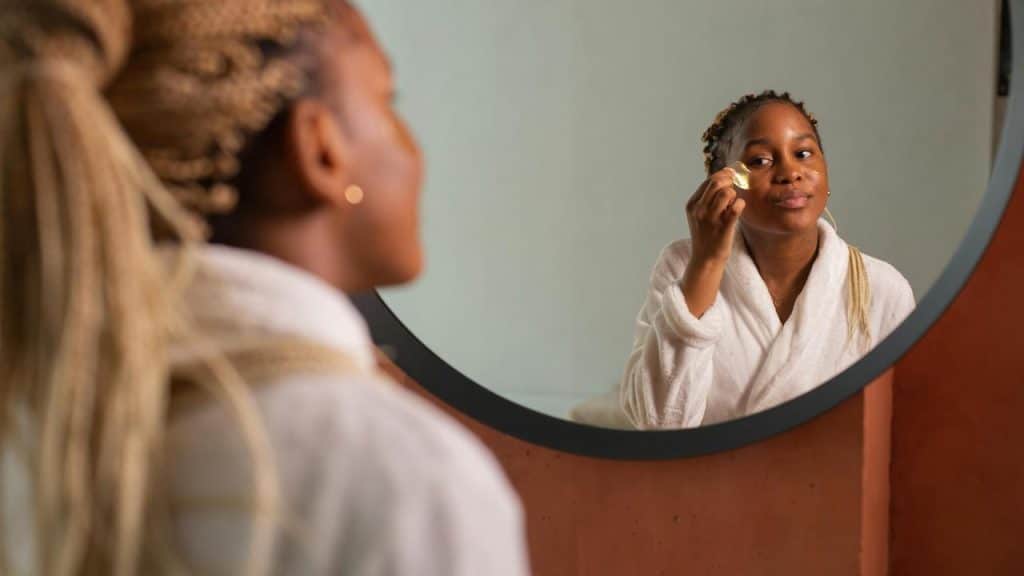 A woman applying skincare under her eyes while looking in the mirror.