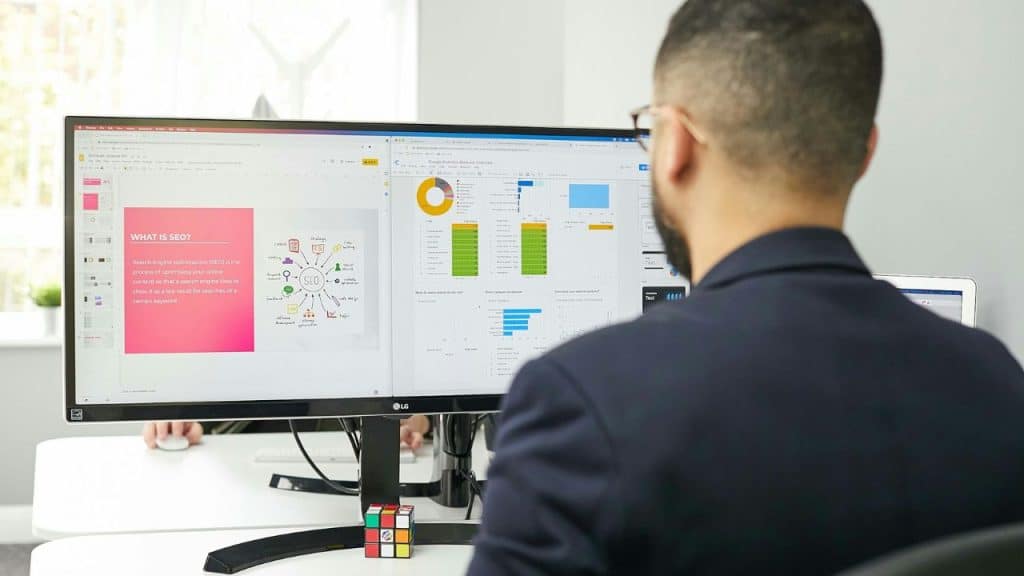 Man viewing a computer monitor displaying a presentation and data charts on a desk.