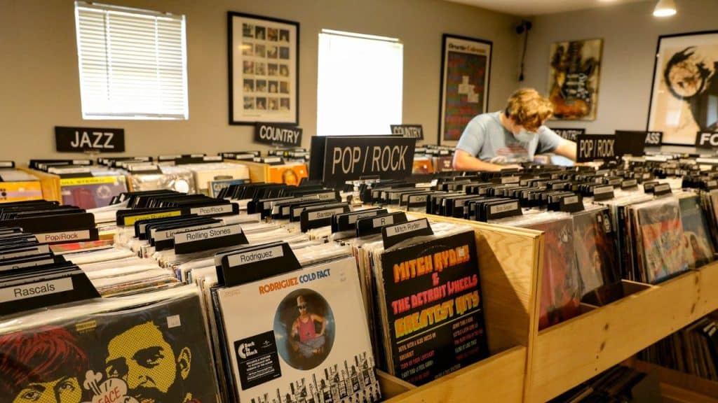 Man browsing shelves of vinyl records categorized by genre in a music store.