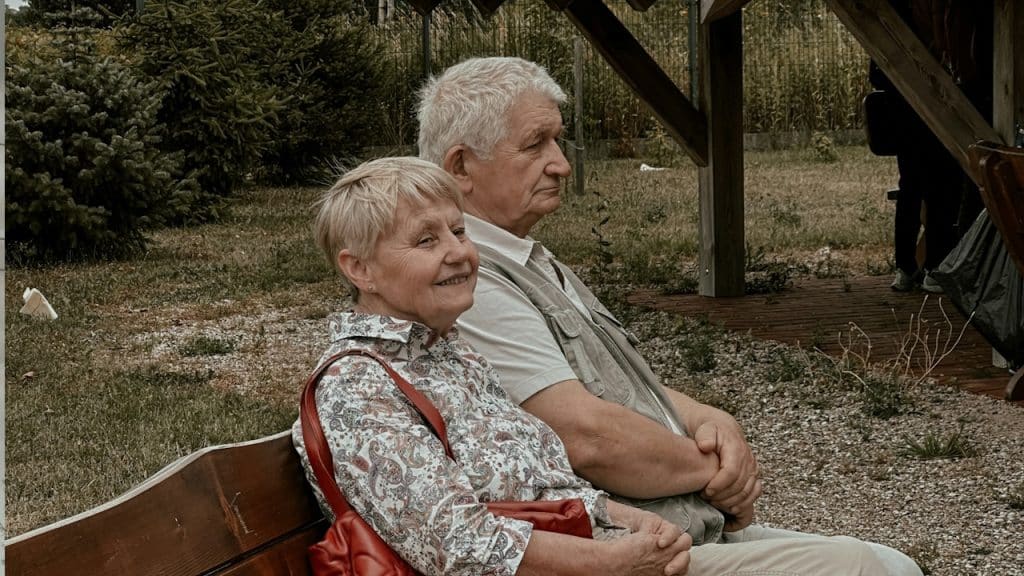 An Old couple sitting silent on a bench, outside their home.