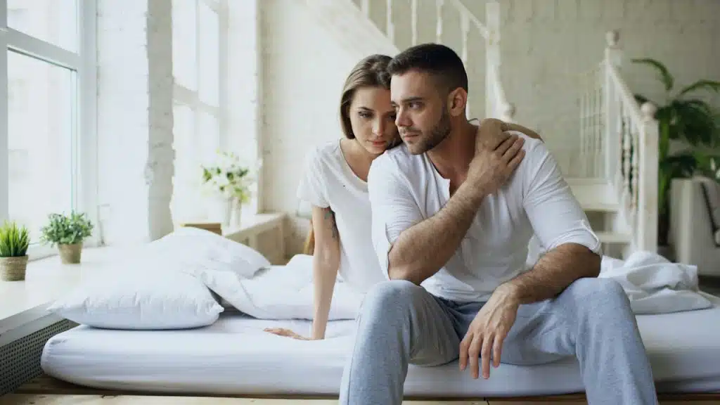 A sad couple sitting together on a bed.