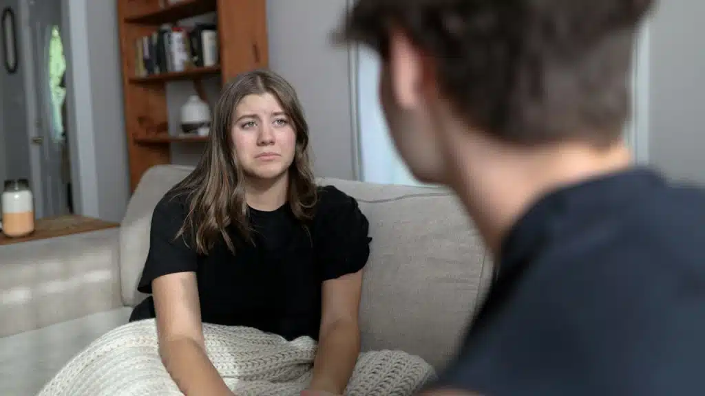 A worried woman sitting on a couch in front of a man.