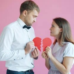 Couple holding broken heart halves on pink background.