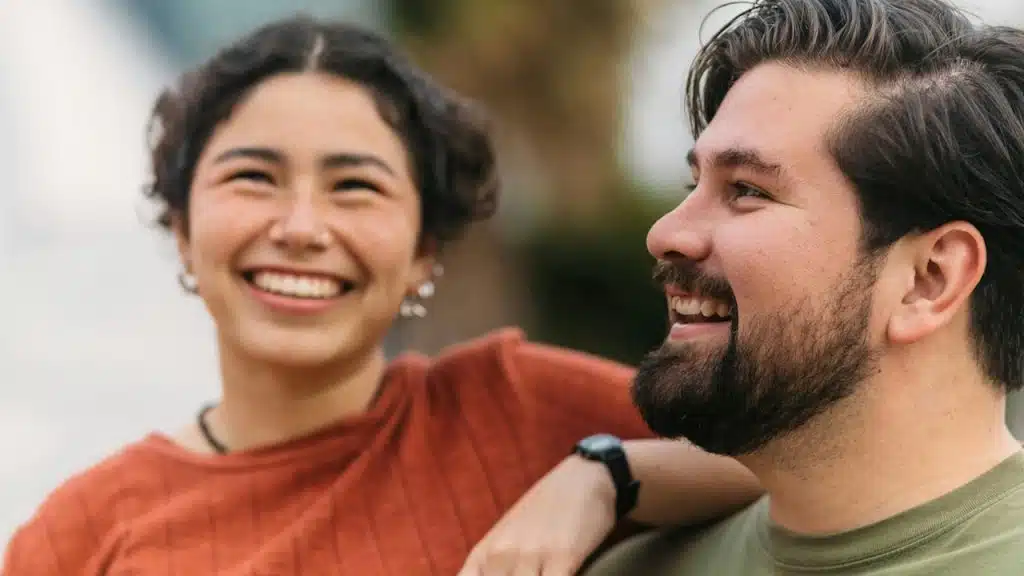 A smiling couple with the woman placing her arm on the manโs shoulder.