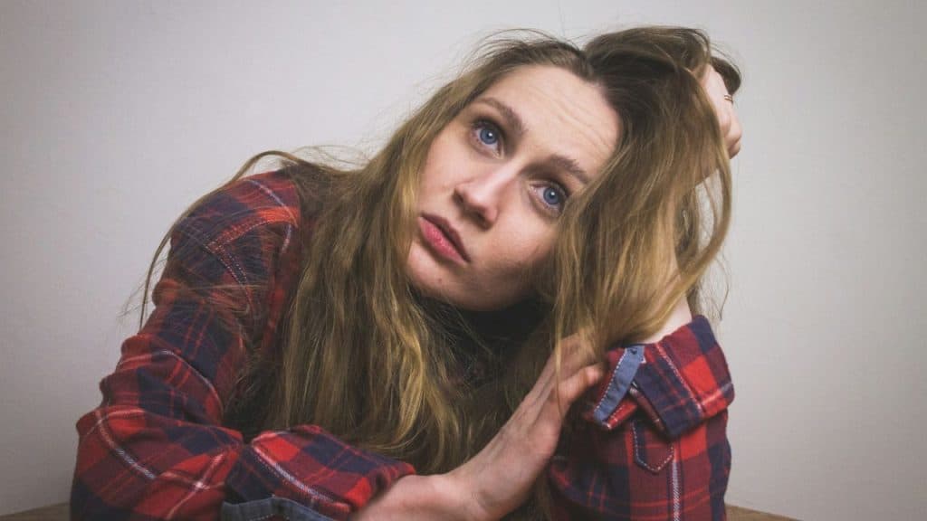 A woman in a red plaid shirt rests her head on her hand, looking directly at the camera.