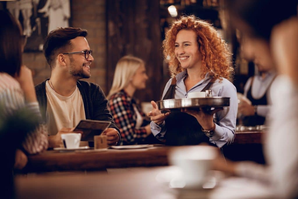 A smiling female student is serving customers in the bar.