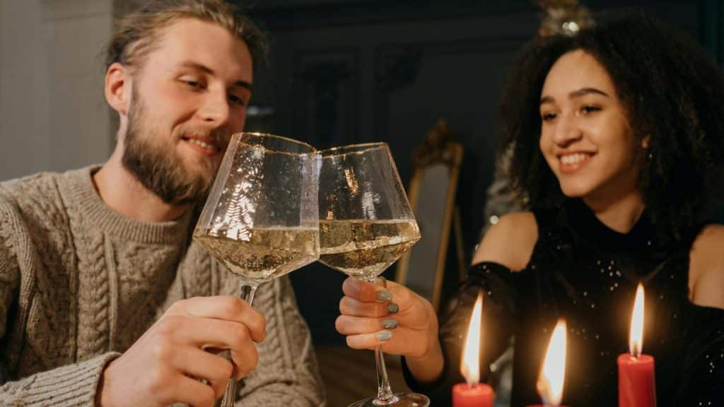 A couple smiling and clinking wine glasses at a candlelit table.