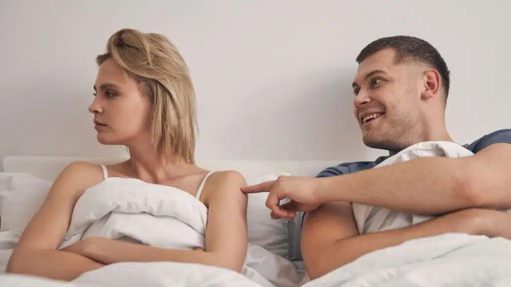 A man touching a woman's arm in bed; she looks away with her arms crossed.