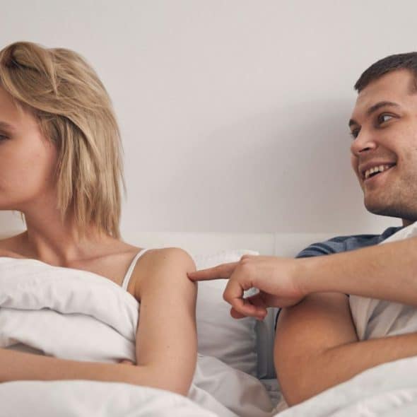 A man touching a woman's arm in bed; she looks away with her arms crossed.
