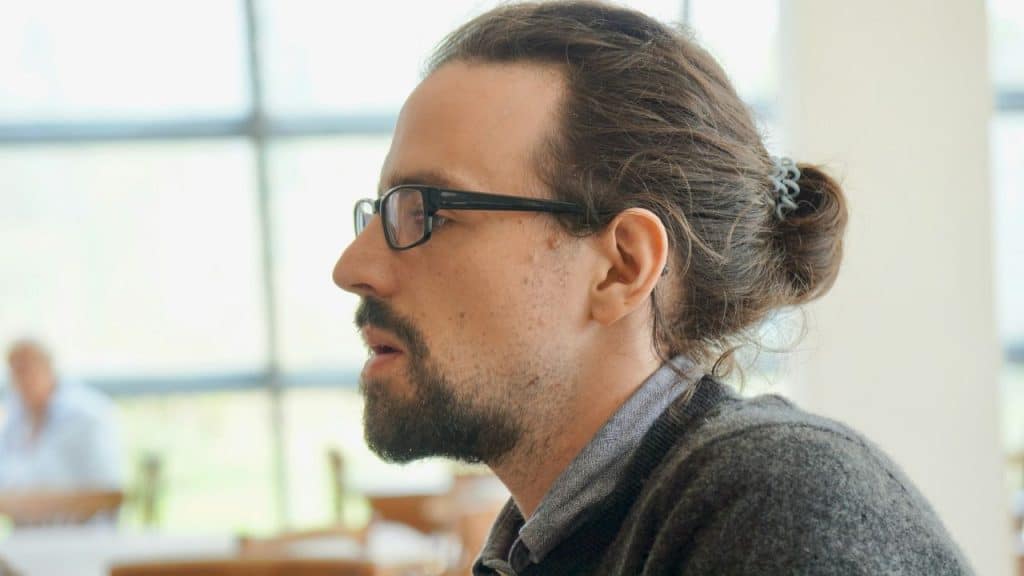 Side view of a man with glasses and a beard, hair in a bun.