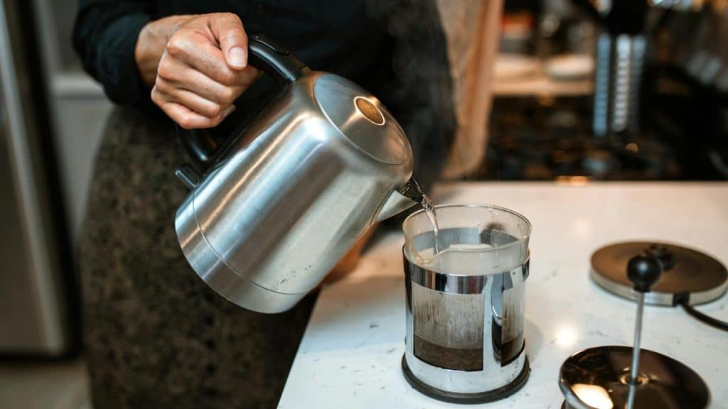 A person pouring hot water from a kettle into a French press.