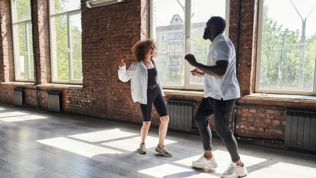 A man and woman dancing together in a bright studio with large windows.