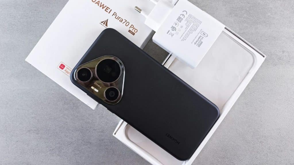 A black smartphone with a large camera module sits on an open box next to a white power adapter.