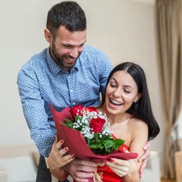 Smiling man giving a bouquet of red roses and baby's breath to a surprised and happy woman.