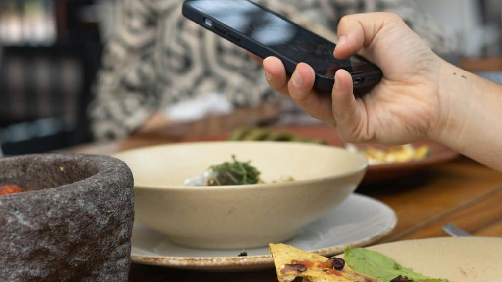 A person taking a photo of their meal with a smartphone at a restaurant table.