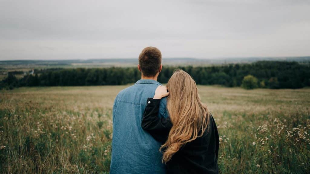 A couple standing in a field with their backs to the camera, looking at the landscape.