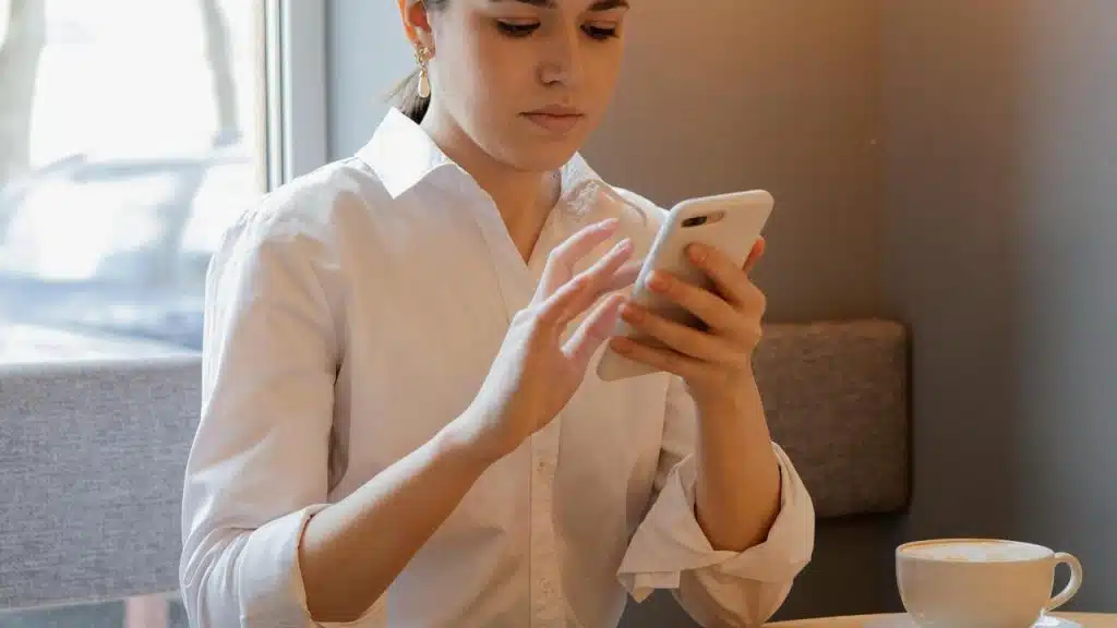 A woman using her smartphone while sitting at a cafe table with a cup of coffee.