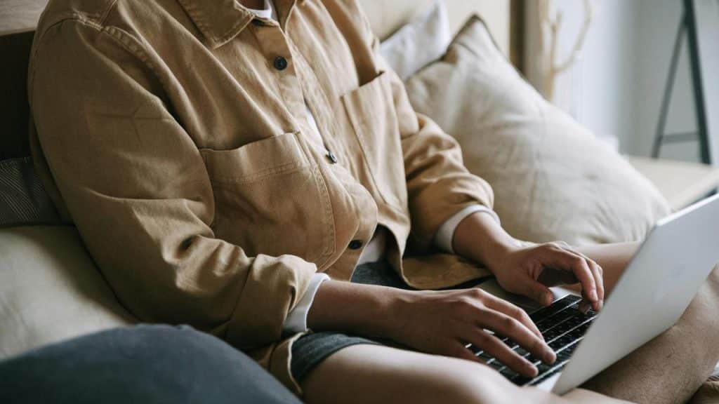 A person sitting on a couch and typing on a laptop.