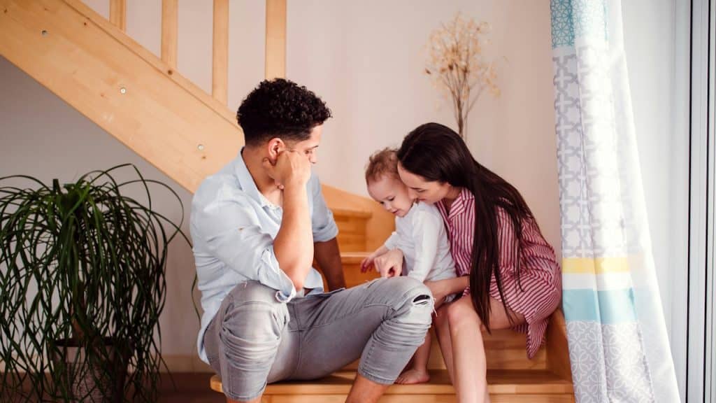 A young couple with their toddler sitting at the bottom of stairs.