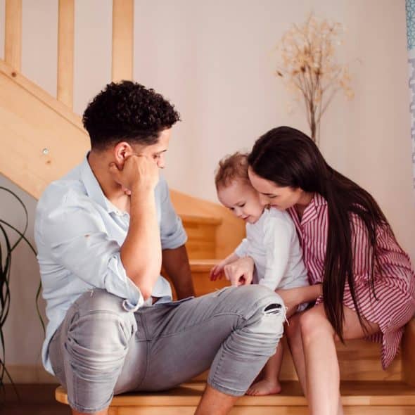 A young couple with their toddler sitting at the bottom of stairs.