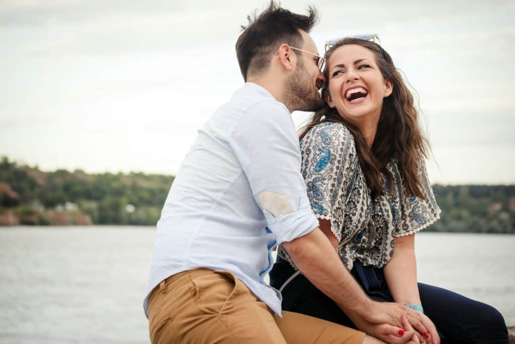 The man is whispering something to the woman that makes her laugh.