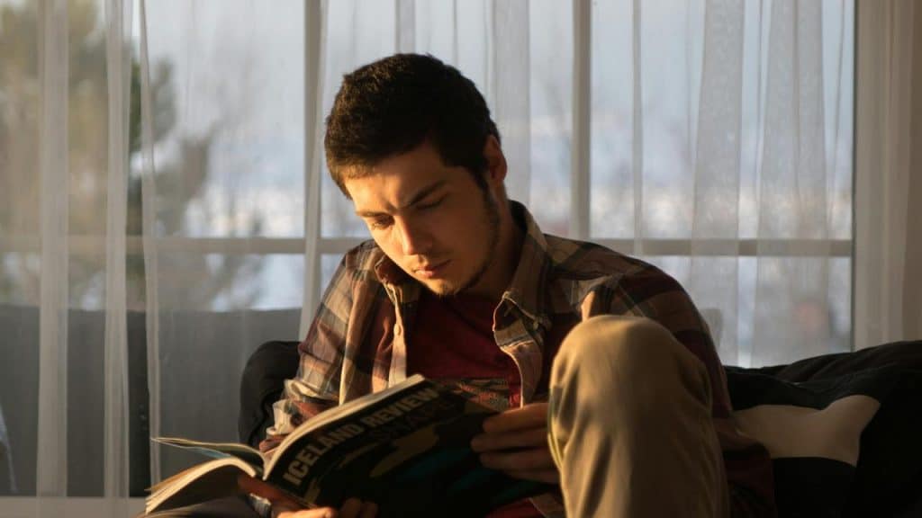 A man sitting by a window reading a magazine.