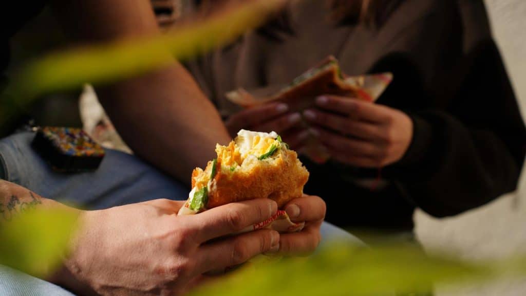 A close-up of two people holding and eating sandwiches.