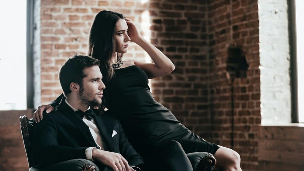 A young couple in formal dress sitting on a chair together.