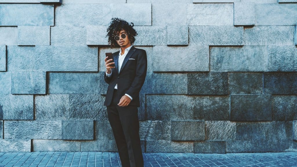 A young man with curly hair standing in front of a textured wall.