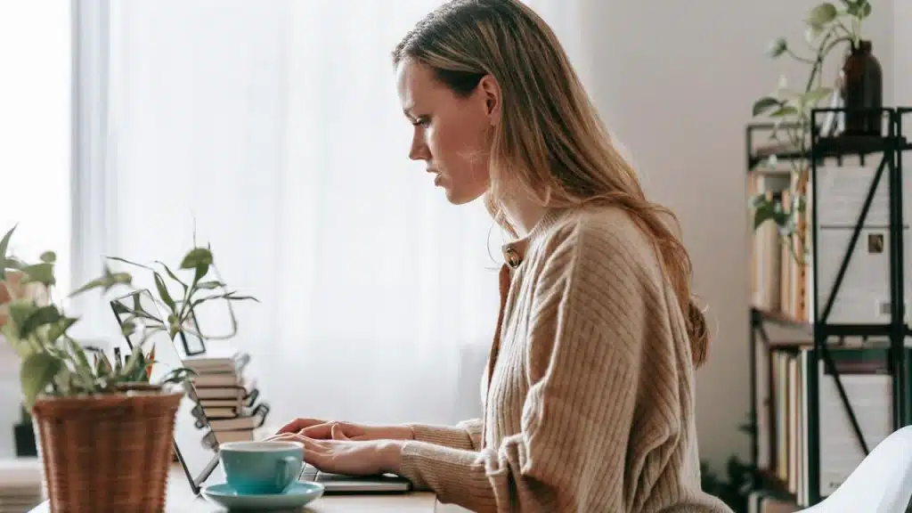 A woman working on a laptop at a desk with plants.