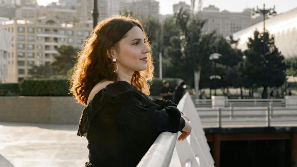 A woman leaning on a railing while looking into the distance outdoors.