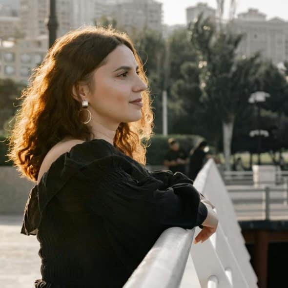 A woman leaning on a railing while looking into the distance outdoors.