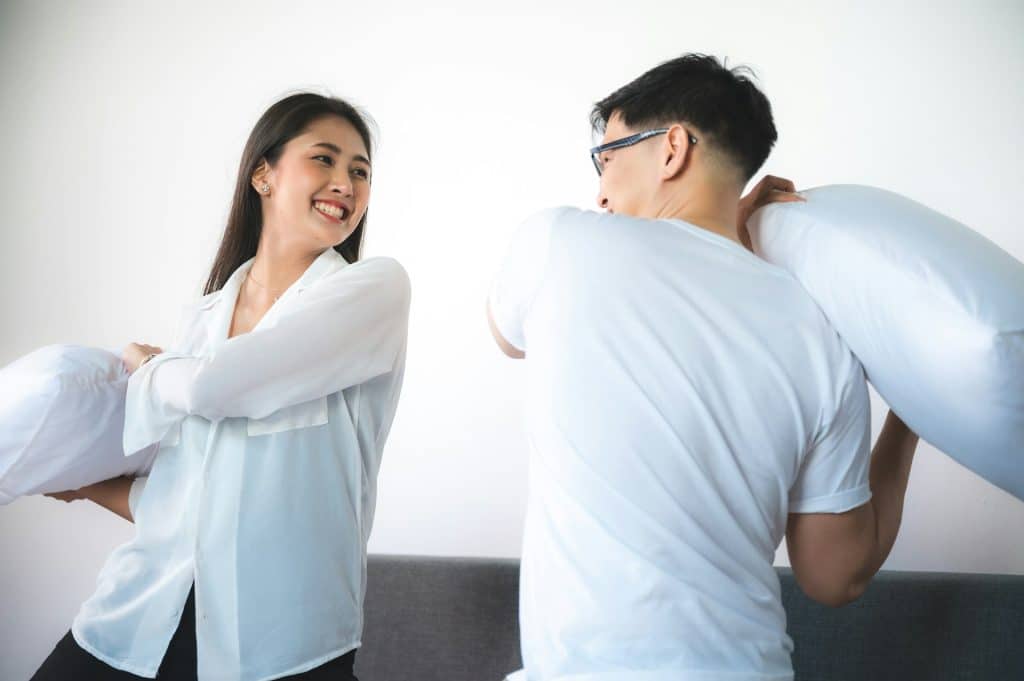 The Asian couple is having a pillow fight in the bedroom.