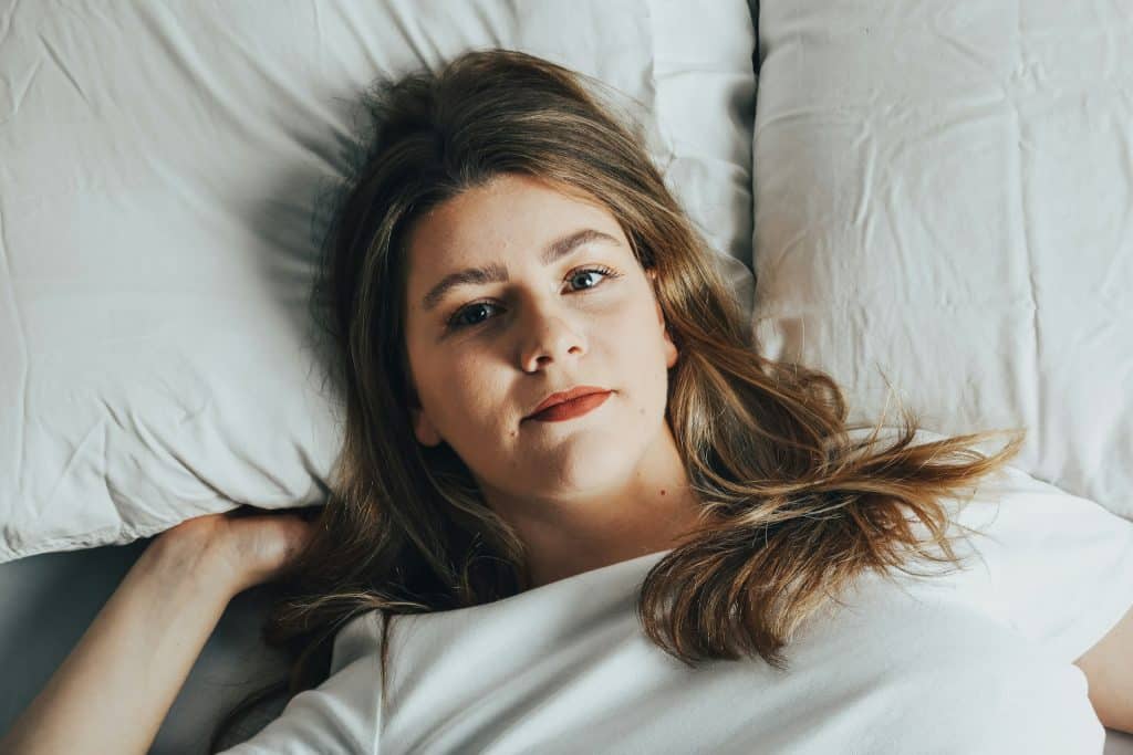The woman is lying on the bed with white sheets.